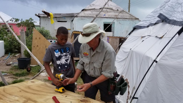 Donnie-teaching-kid-to-drill-in-front-of-damaged-home